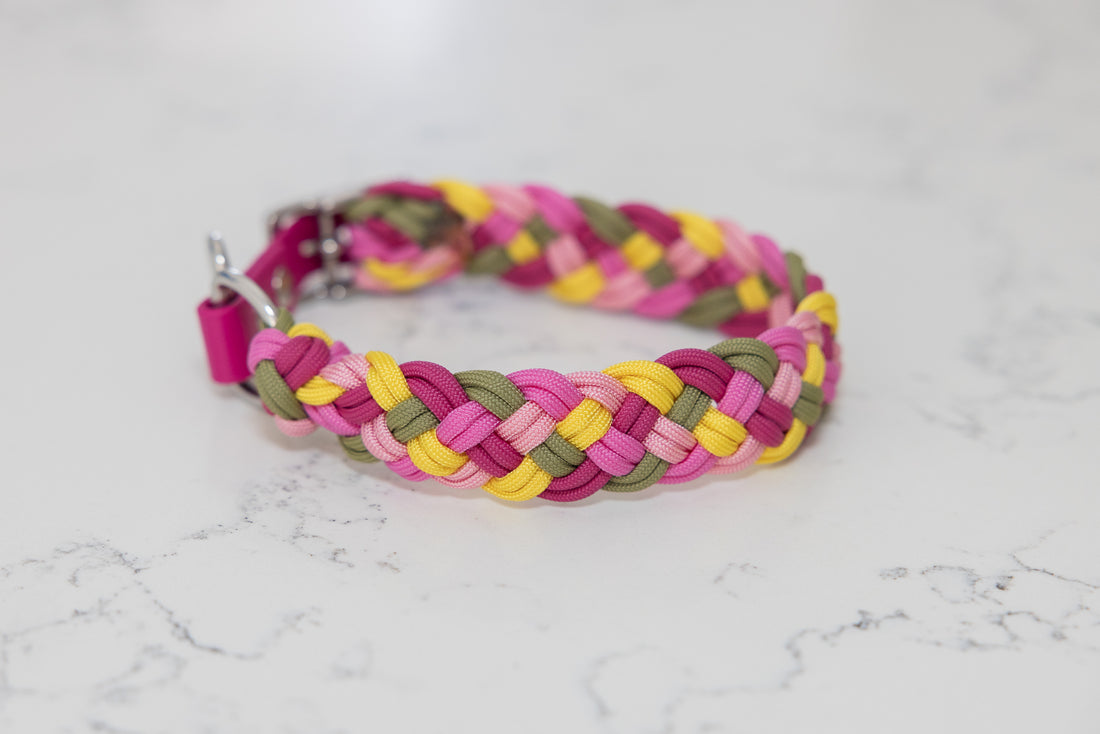A multicolored paracord dog collar with pink, yellow, and green strands, displayed on a marble background.