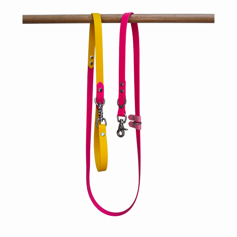 Yellow and pink Biothane dog lead on a wooden rack against a white background 
